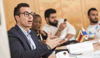 A man with glasses speaking during a meeting.